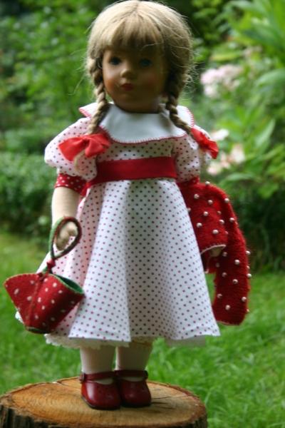 Gritli von Vorne im weißen
                            Baumwollkleid mit roten Punkten, Glockenrock
                            und weißem Baumwollkrägelchen, rotem
                            Mohairjäckchen mit eingestrickten
                            Holzperlen, dazu passend die Tasche